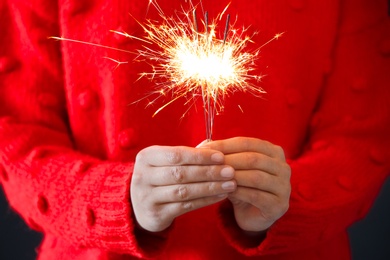 Photo of Woman in red sweater holding burning sparklers, closeup