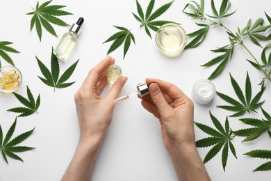 Woman applying CBD oil or THC tincture onto skin at white background, top view