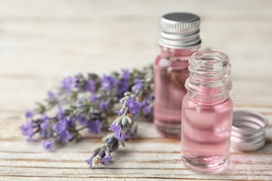 Photo of Bottles with natural lavender essential oil on white wooden background. Space for text