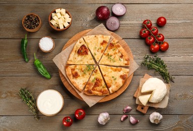 Photo of Delicious khachapuri with cheese, sauce, vegetables and spices on wooden table, flat lay