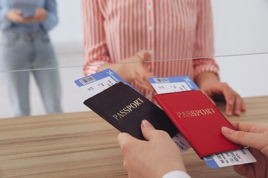 Photo of Agent giving passports with tickets to client at check-in desk in airport, closeup