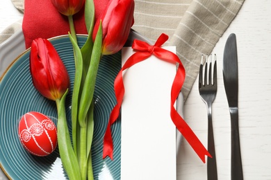 Festive Easter table setting with blank card and flowers on wooden background, top view. Space for text