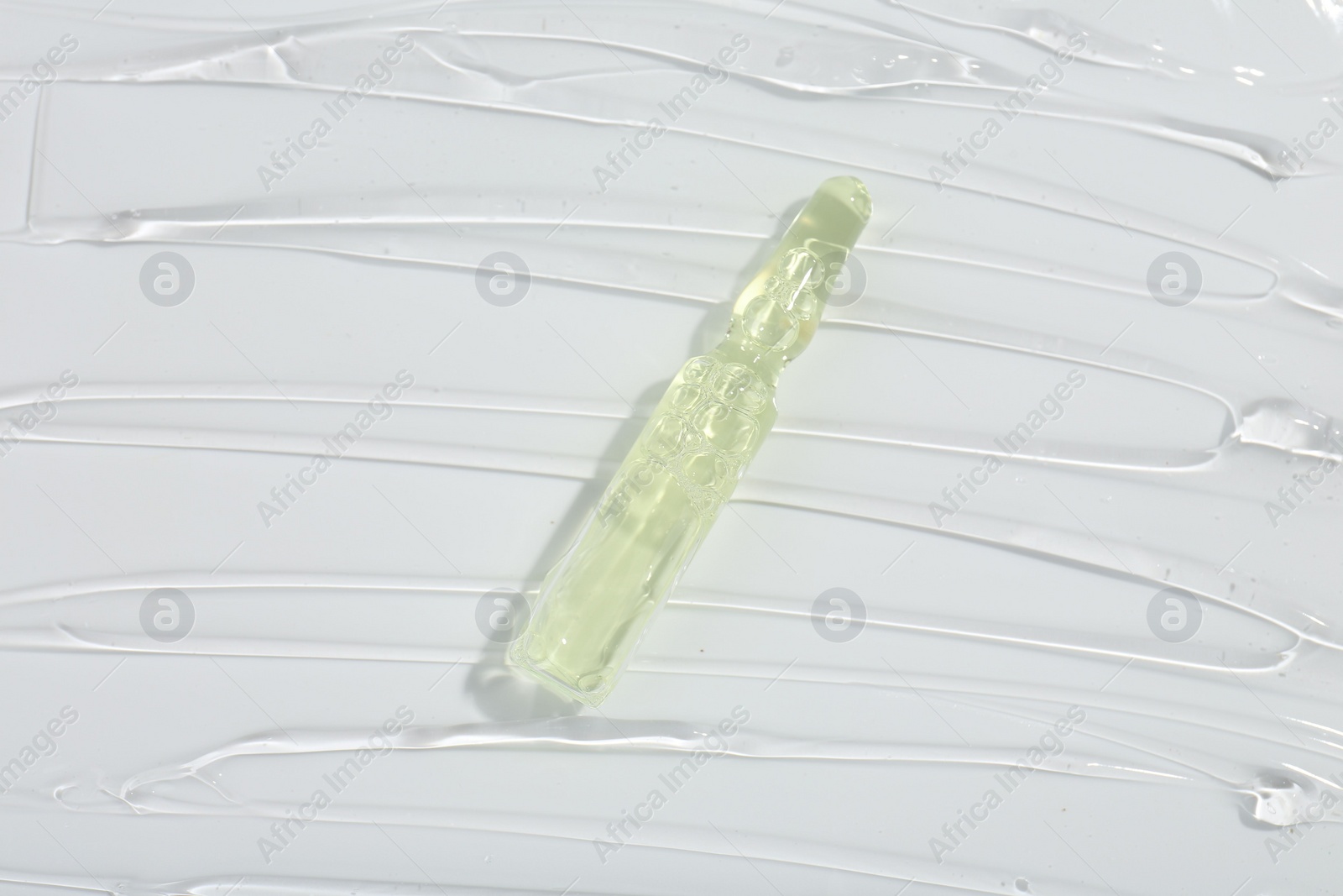 Photo of Skincare ampoule on white surface covered with gel, top view