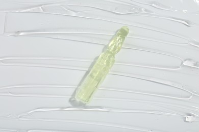 Photo of Skincare ampoule on white surface covered with gel, top view