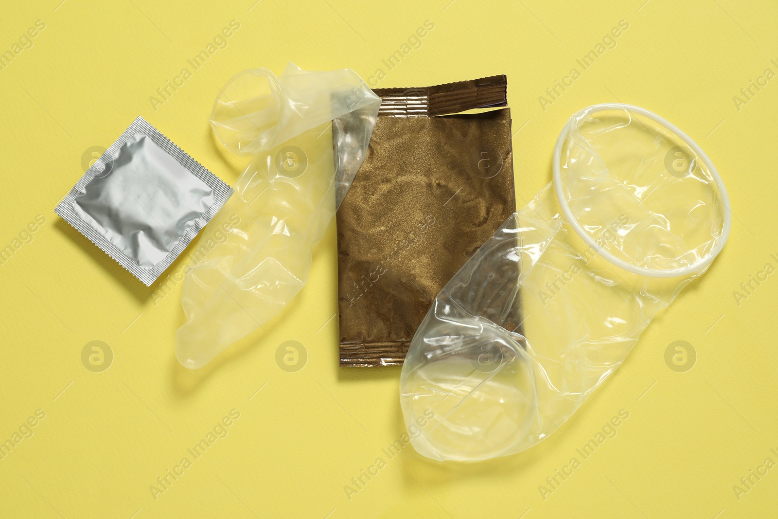 Photo of Unrolled female, male condoms and packages on yellow background, flat lay. Safe sex