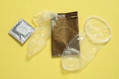 Photo of Unrolled female, male condoms and packages on yellow background, flat lay. Safe sex