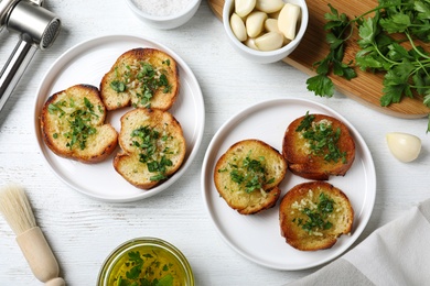 Photo of Slices of toasted bread with garlic and herb on white wooden table, flat lay