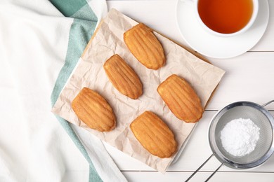 Photo of Tasty madeleine cookies, tea and powdered sugar on white wooden table, flat lay