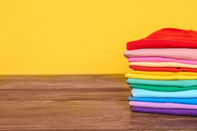 Photo of Stack of colorful t-shirts on table against color background