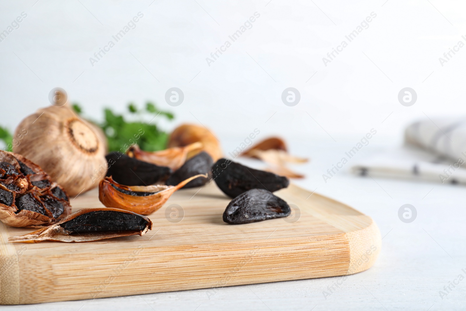 Photo of Wooden board with black garlic on white table. Space for text