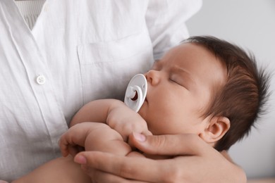 Mother holding her cute little baby with pacifier on light background, closeup