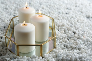 Tray with three white burning candles on rocks. Space for text