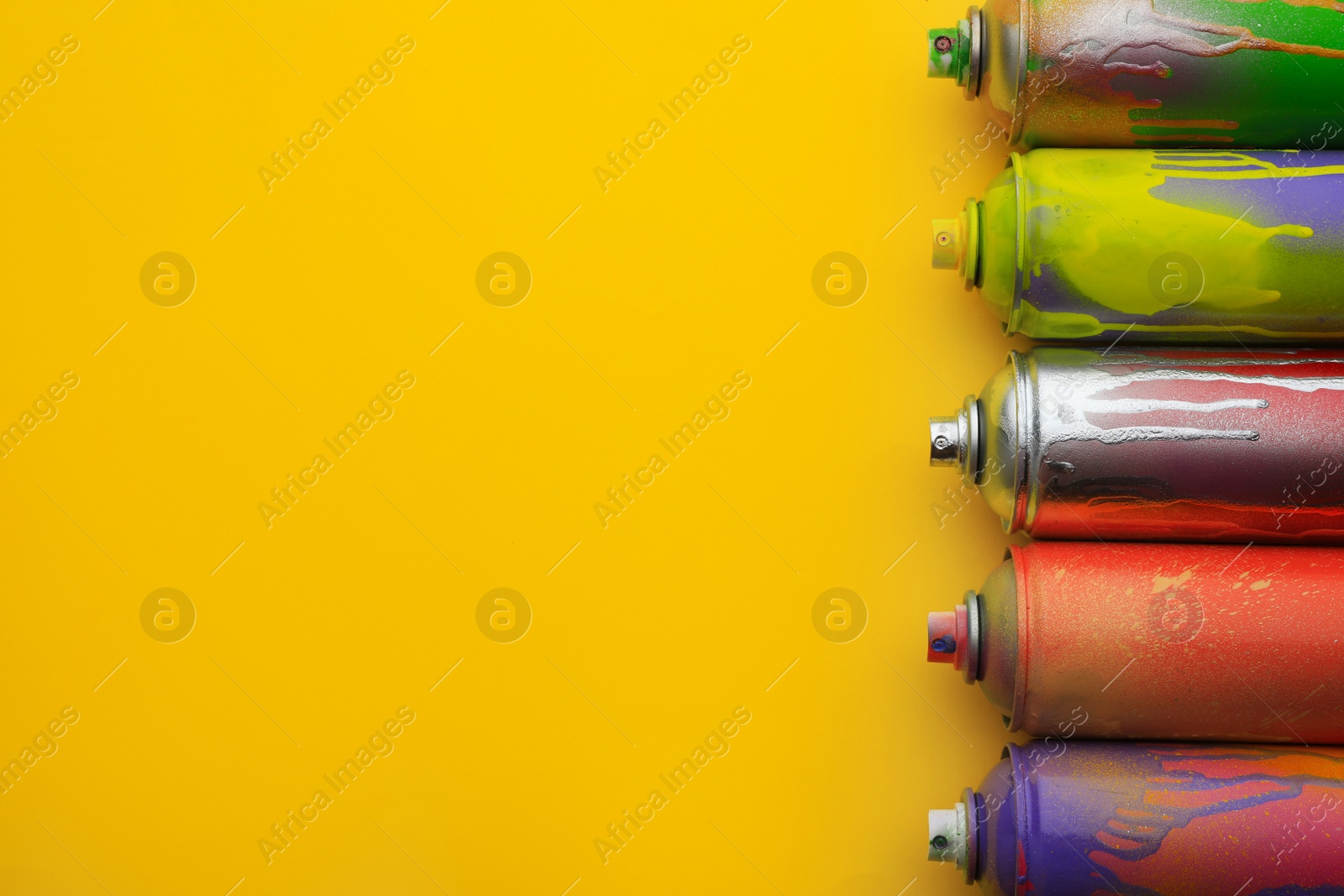 Photo of Used cans of spray paints on yellow background, flat lay with space for text. Graffiti supplies