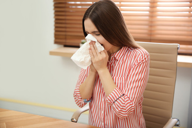 Photo of Sick young woman sneezing at workplace. Influenza virus