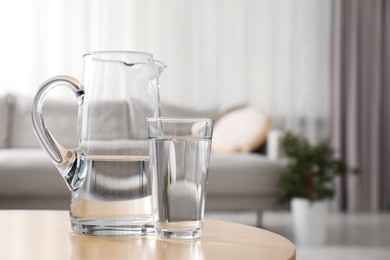 Photo of Jug and glass with clear water on table indoors, closeup. Space for text