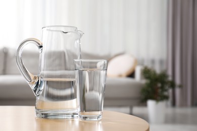 Jug and glass with clear water on table indoors, closeup. Space for text