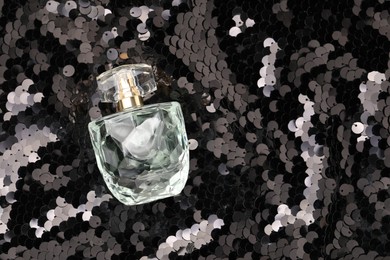 Luxury perfume in bottle on fabric with shiny sequins, top view