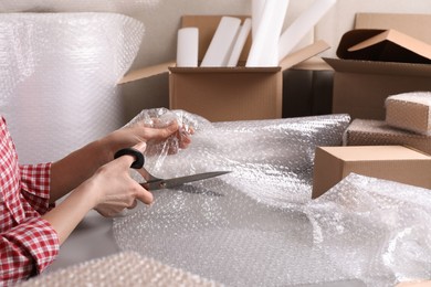 Photo of Woman cutting bubble wrap at table in warehouse, closeup