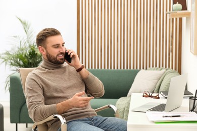 Photo of Young man talking on phone while working at home, space for text