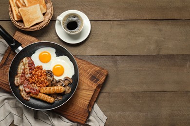 Photo of Frying pan with cooked traditional English breakfast and cup of coffee on wooden table, flat lay. Space for text