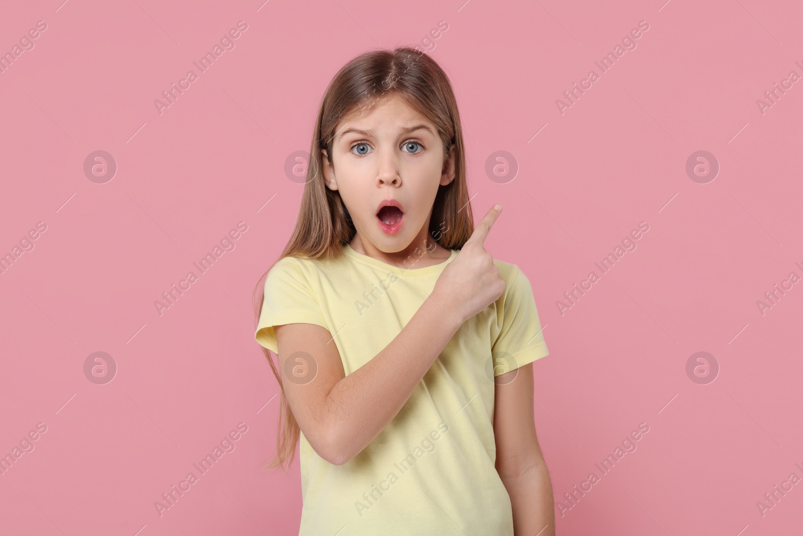 Photo of Surprised girl pointing at something on pink background
