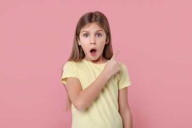 Photo of Surprised girl pointing at something on pink background
