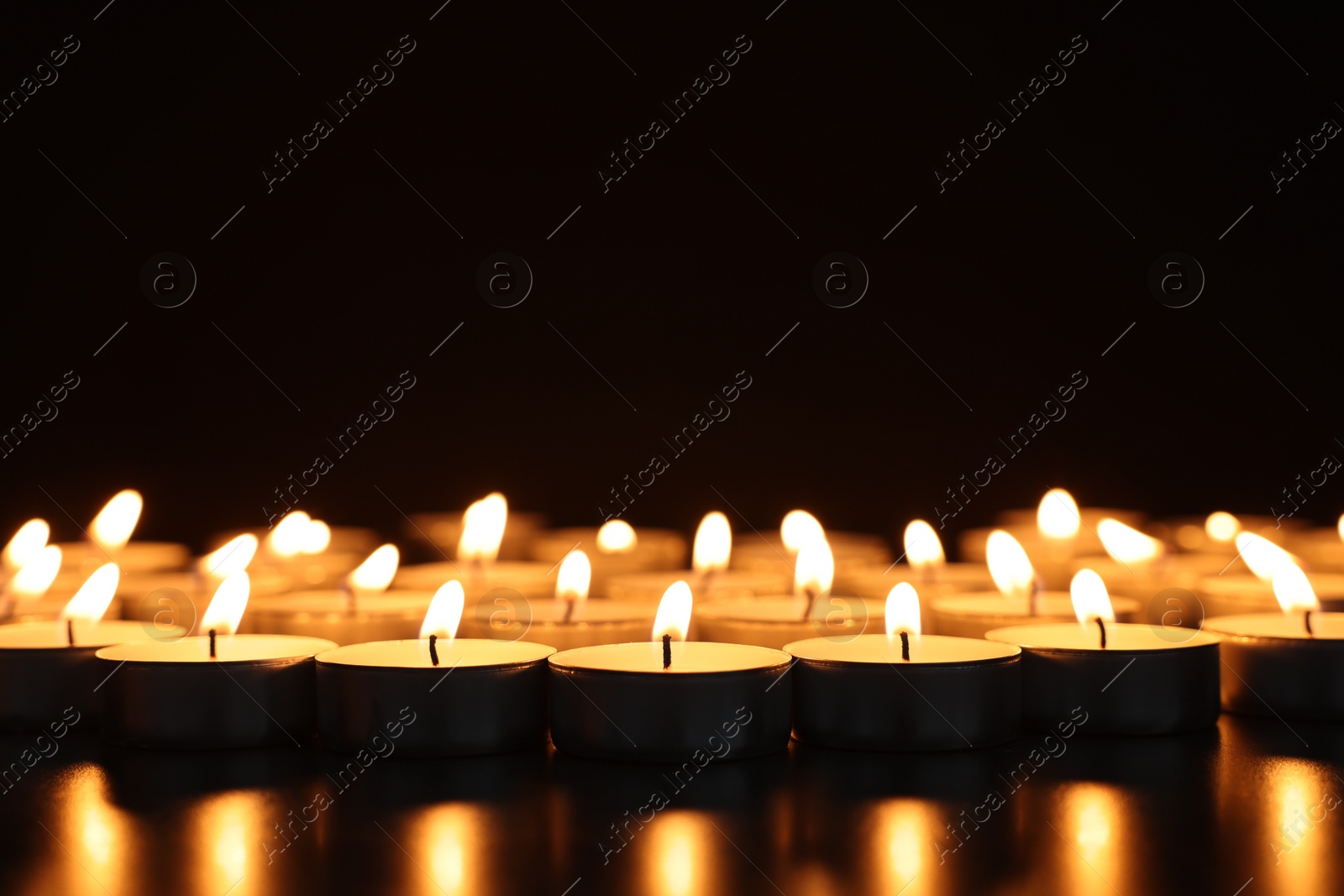 Photo of Burning candles on dark surface against black background, closeup. Space for text