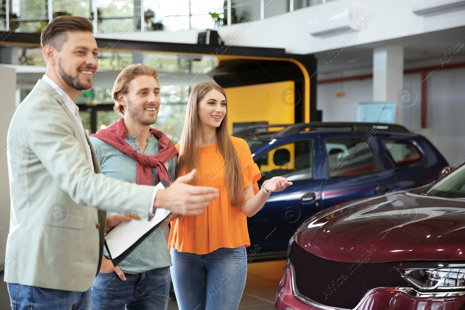 Photo of Salesman with clipboard consulting young couple in modern car dealership