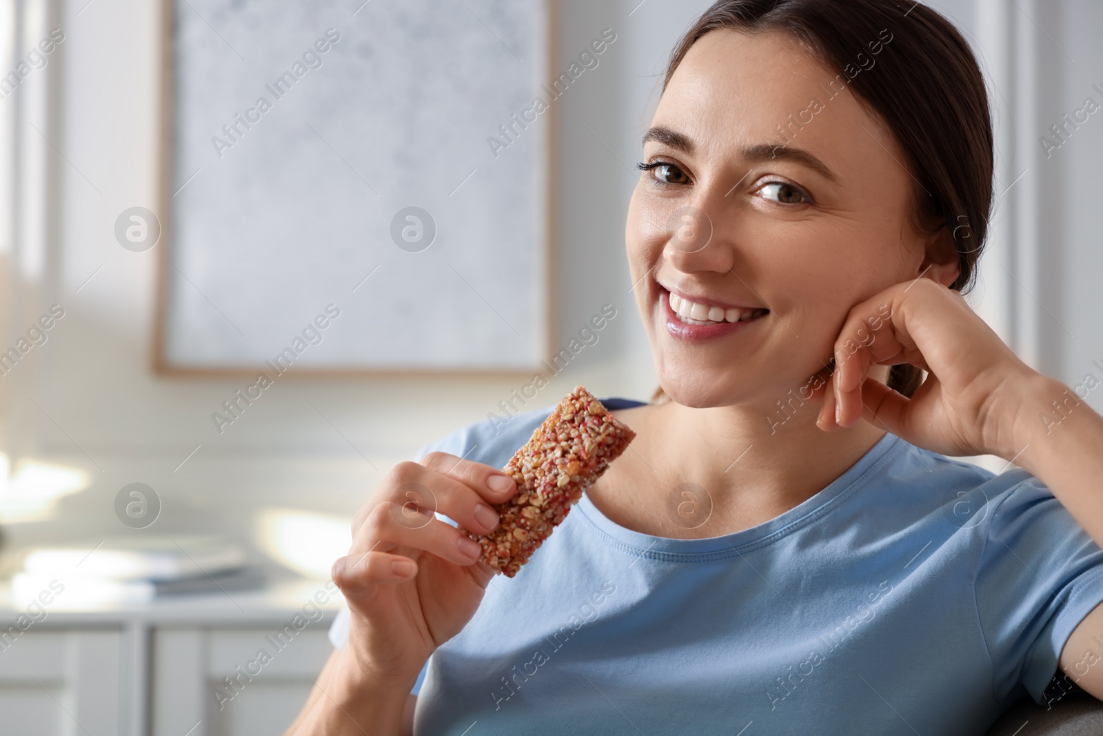 Photo of Woman holding tasty granola bar at home