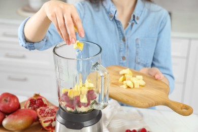 Photo of Woman adding mango into blender with ingredients for smoothie indoors, closeup