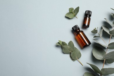 Aromatherapy. Bottles of essential oil and eucalyptus leaves on light grey background, flat lay. Space for text