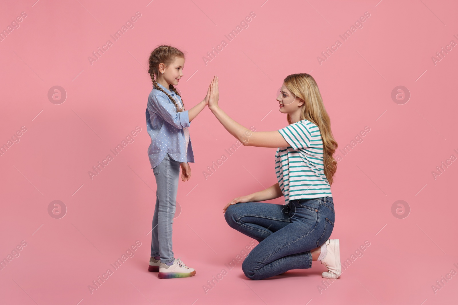 Photo of Mother and daughter giving high five on pink background