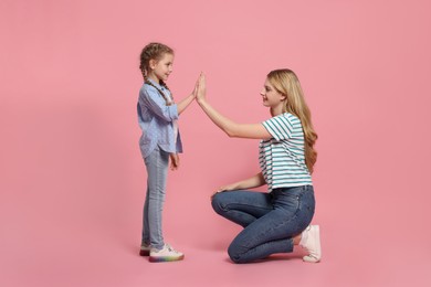 Mother and daughter giving high five on pink background