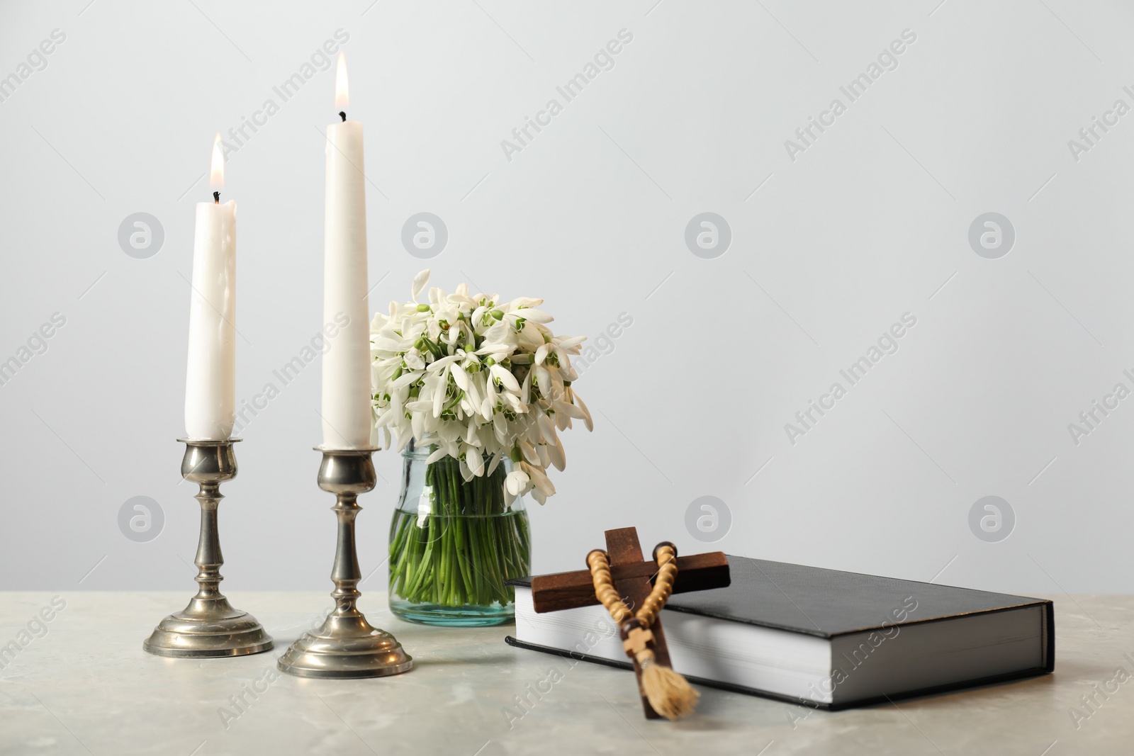 Photo of Church candles, wooden cross, rosary beads, Bible and flowers on marble table. Space for text