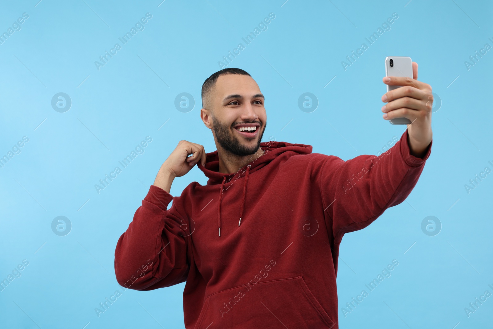 Photo of Smiling young man taking selfie with smartphone on light blue background