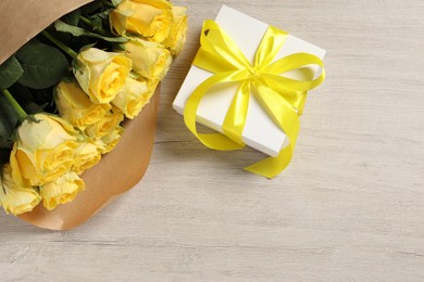 Photo of Beautiful bouquet of yellow roses and gift box on wooden table, flat lay. Space for text