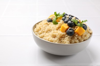 Photo of Tasty quinoa porridge with blueberries, pumpkin and mint in bowl on white table