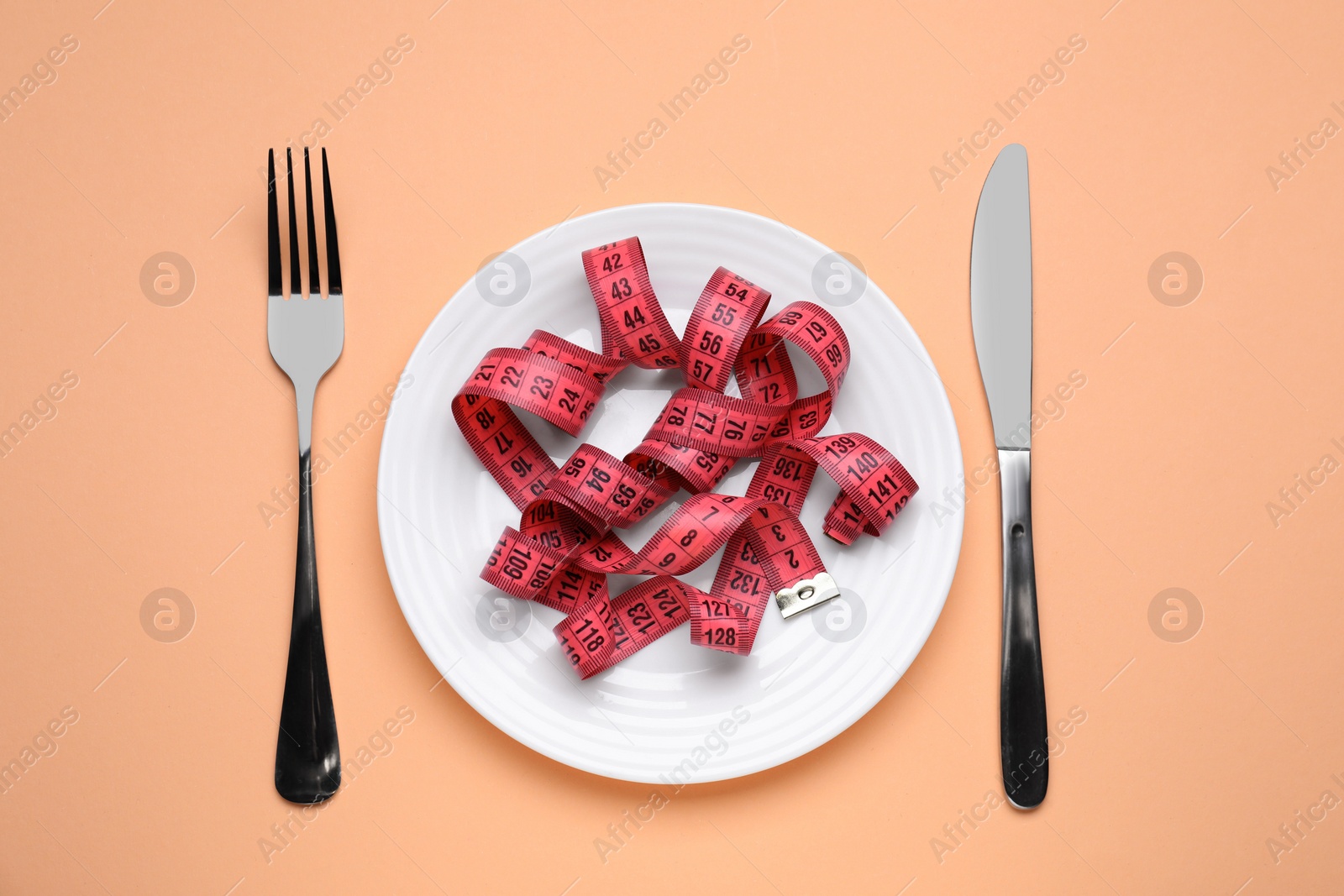 Photo of Measuring tape, fork and knife on beige background, flat lay. Weight loss concept