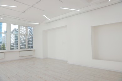 Photo of Empty office room with white walls, clean window and modern lights on ceiling. Interior design