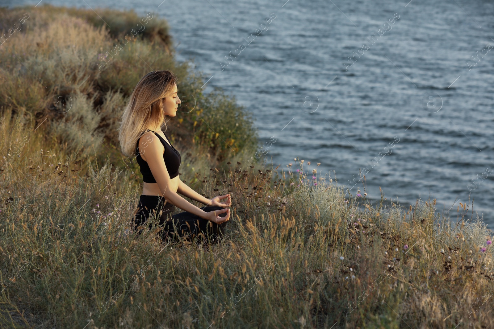 Photo of Young woman meditating near river on sunny day, space for text