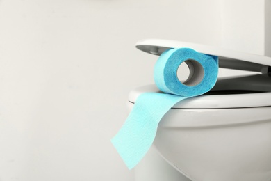 Photo of Toilet bowl with paper roll on light background. Space for text