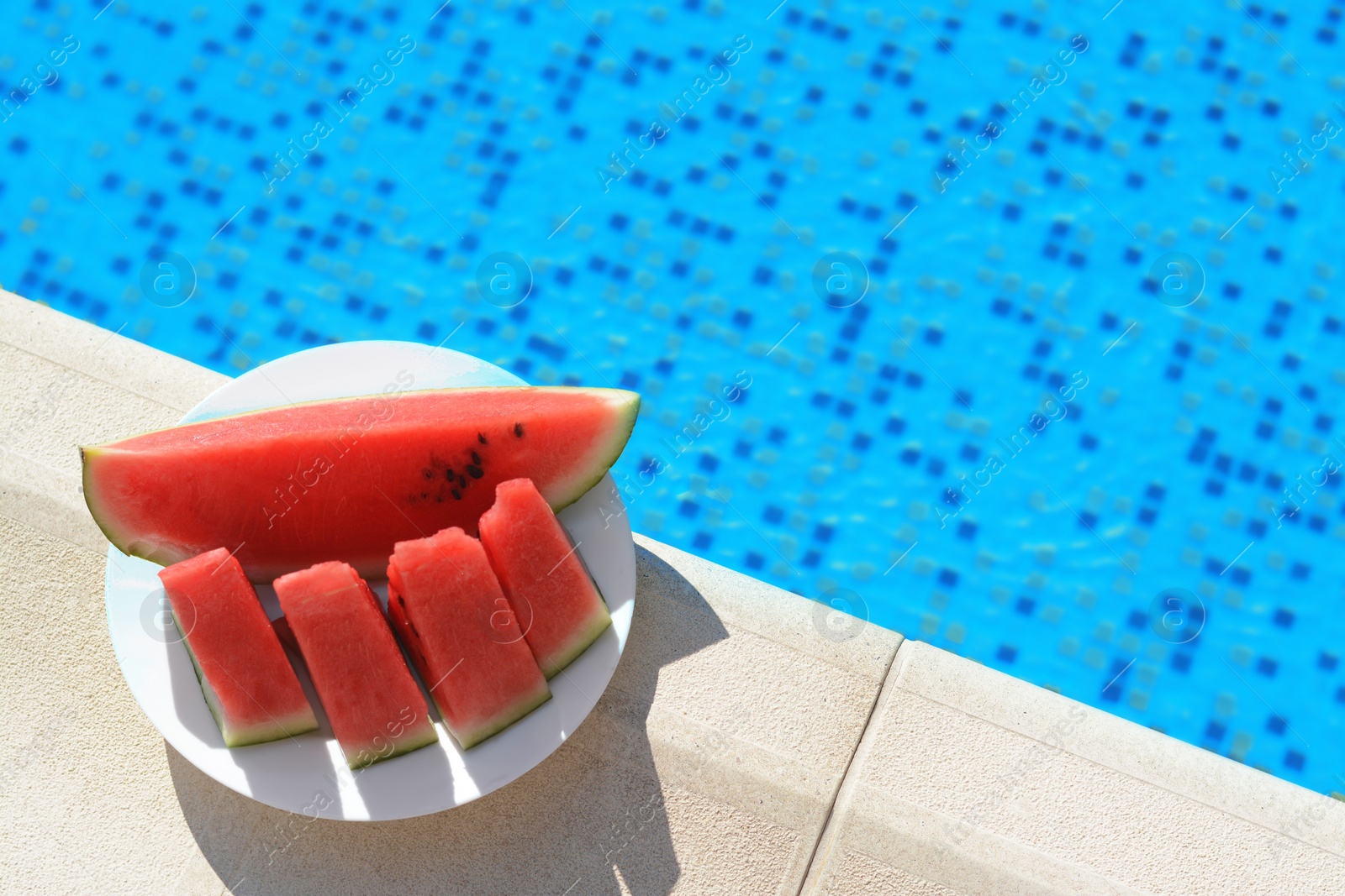 Photo of Slices of watermelon on white plate near swimming pool outdoors, top view. Space for text