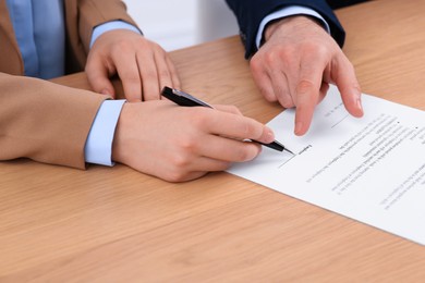 Businesspeople signing contract at wooden table, closeup of hands