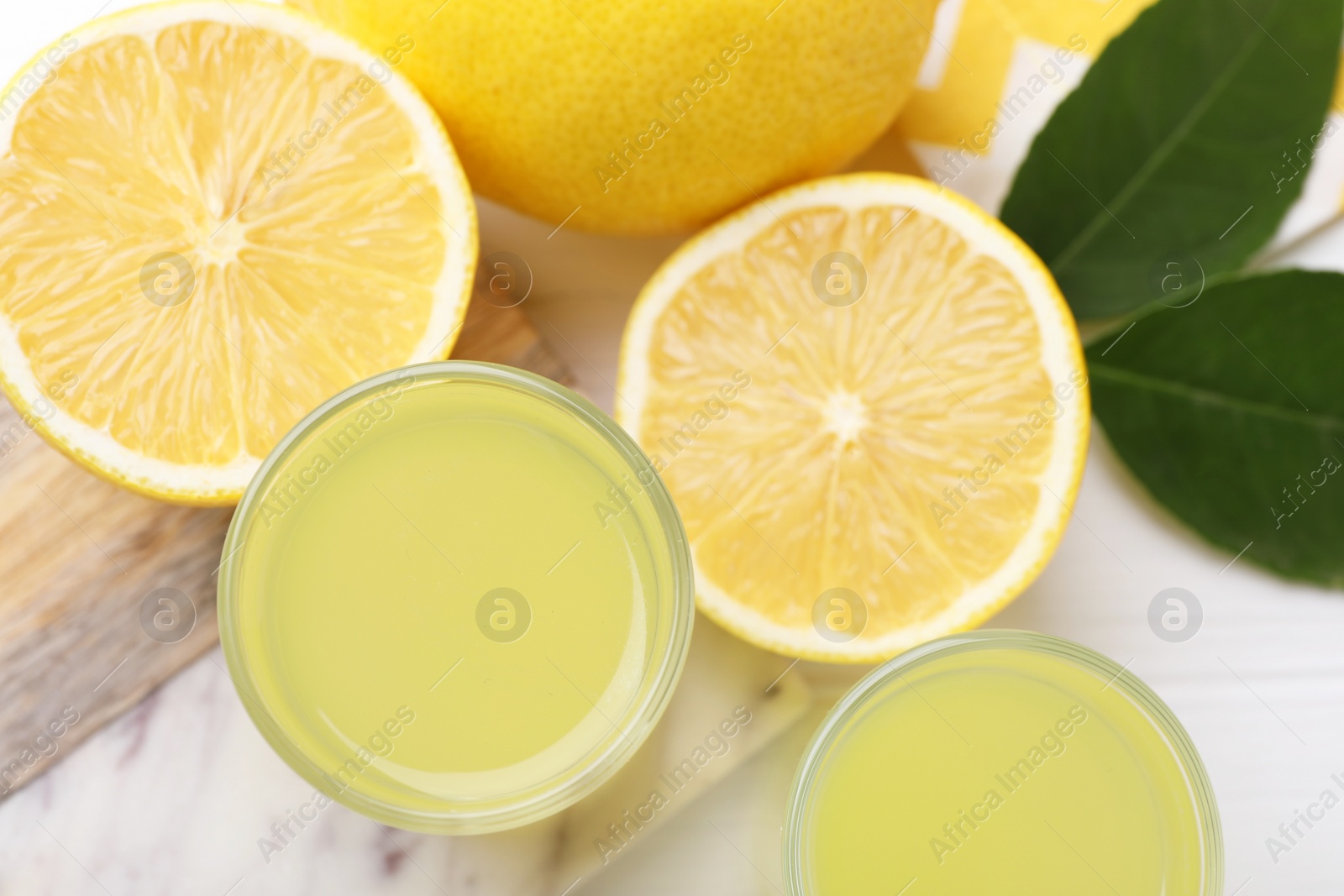 Photo of Tasty limoncello liqueur, lemons and green leaves on table, top view