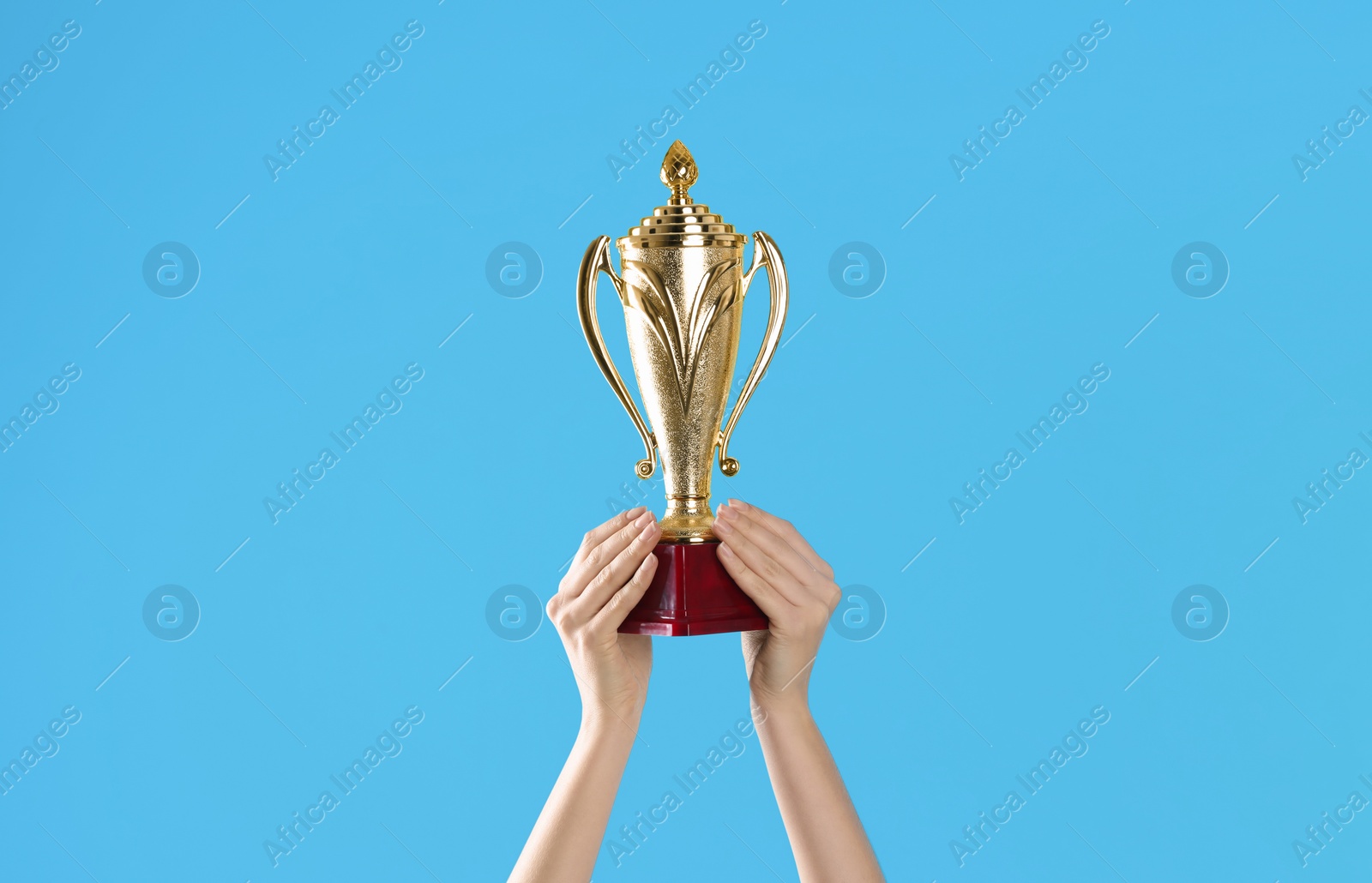 Photo of Woman holding gold trophy cup on light blue background, closeup