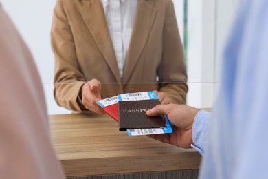 Man giving passports with tickets to agent at check-in desk in airport, closeup