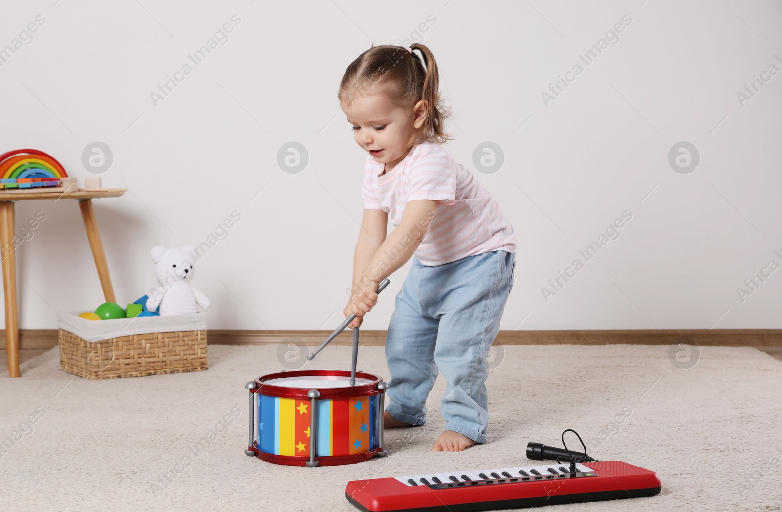 Photo of Cute little girl playing with drum, drumsticks and toy piano at home