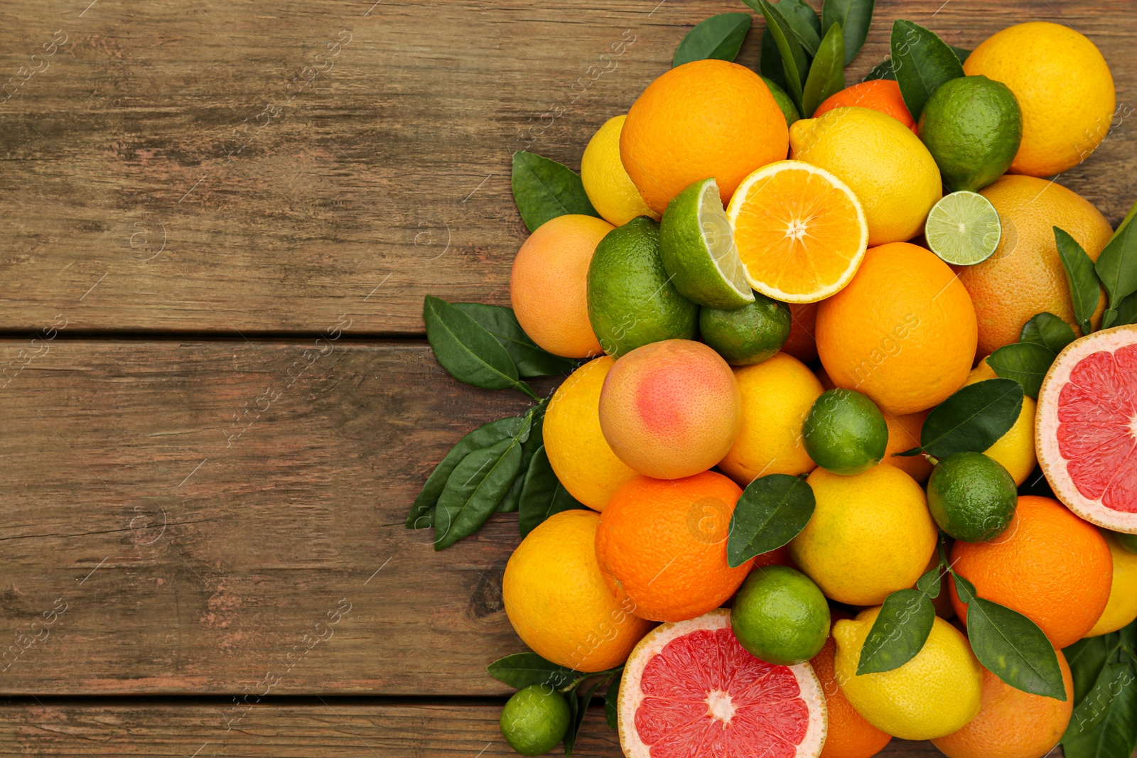 Photo of Different citrus fruits with green leaves on wooden table, flat lay. Space for text