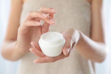 Young woman holding jar of cream at home, closeup