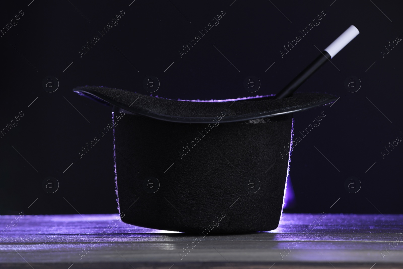 Photo of Magician's hat and wand on wooden table against black background